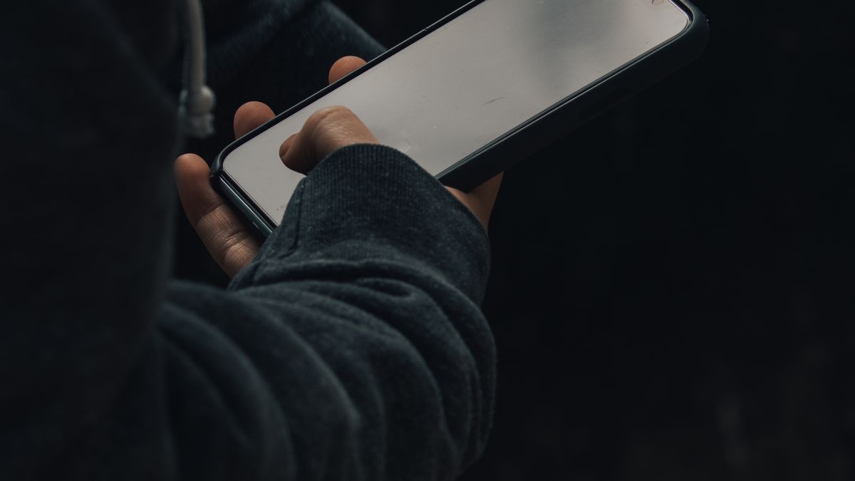 Osoba trzymająca smartfon z wygaszonym ekranem w ciemności