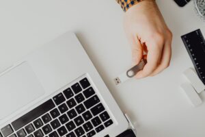 Dłoń trzymająca pendrive USB obok laptopa na białym biurku