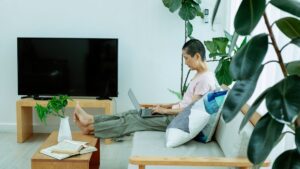 Osoba z laptopem na kanapie w salonie, naprzeciwko telewizor