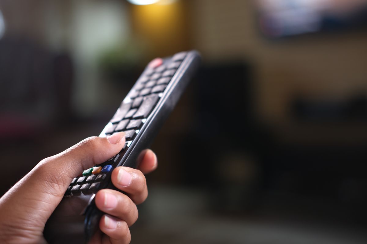 Dłoń trzymająca pilot do telewizora w salonie