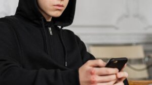 Nastolatek w bluzie z kapturem czytający wiadomości na telefonie