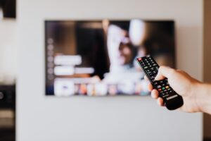 Dłoń kierująca pilot w stronę telewizora zawieszonego na ścianie