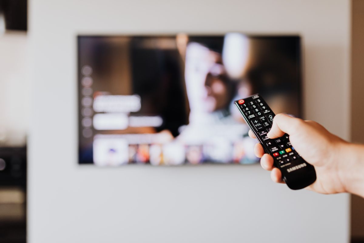 Dłoń kierująca pilot w stronę telewizora zawieszonego na ścianie