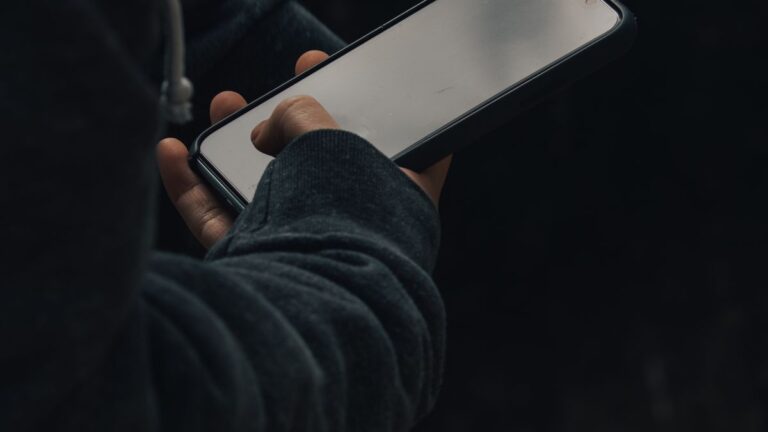 Osoba trzymająca smartfon z wygaszonym ekranem w ciemności