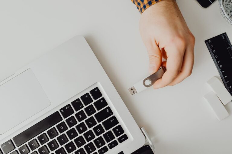 Dłoń trzymająca pendrive USB obok laptopa na białym biurku