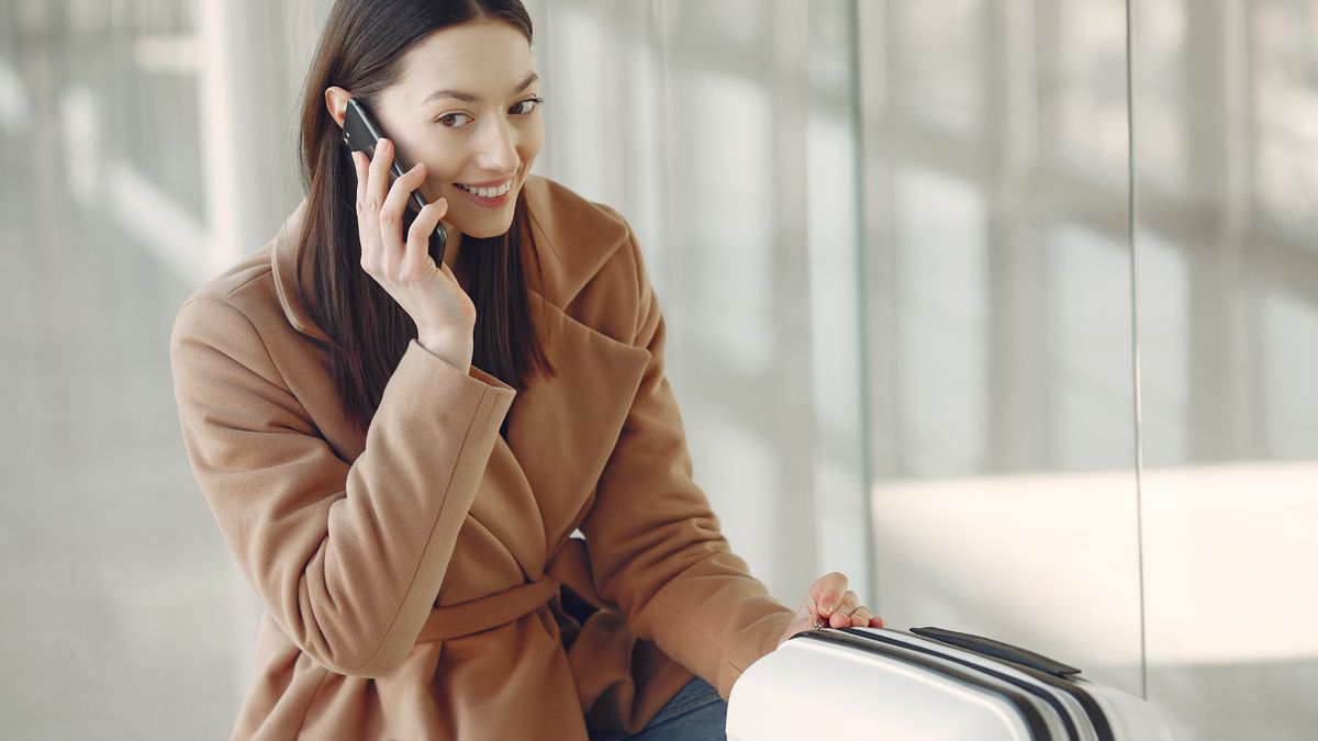 Podróżna rozmawiająca przez telefon z walizką na dworcu