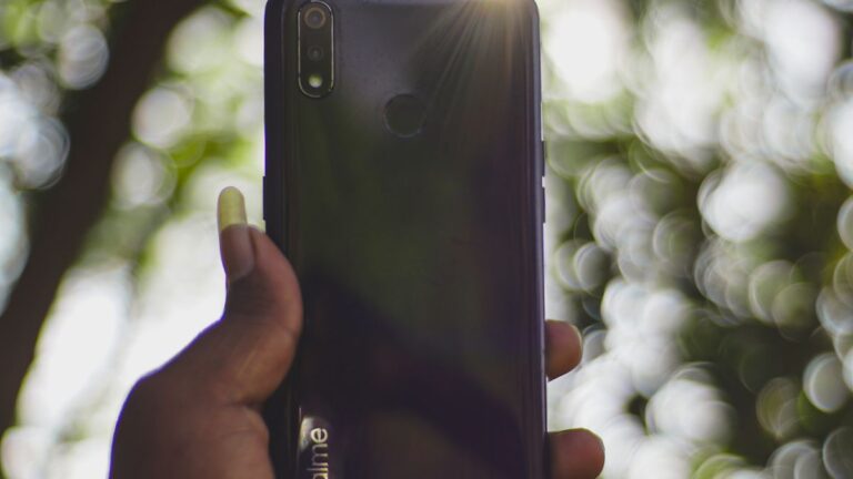 Telefon trzymany w dloni w ostrym sloncu pod drzewem